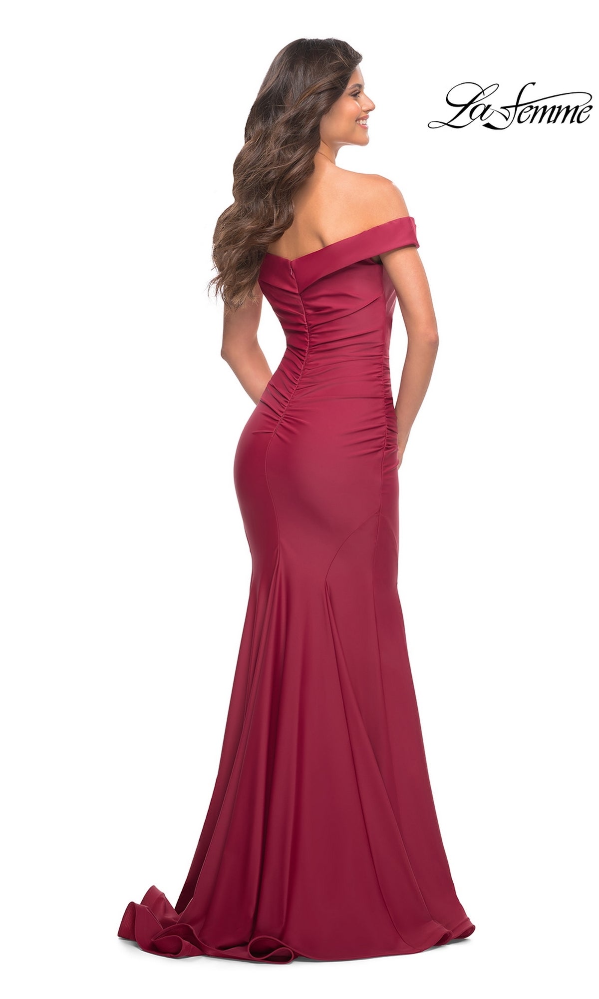 A woman faces away from the camera in a La Femme Off-the-Shoulder Long Formal Prom Gown, showcasing its fitted floor-length burgundy silhouette and ruched back detailing.
